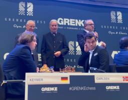 Wolfgang Grenke (stehend links) führt gleich den symbolischen ersten Zug des Turniers am Brett von Vincent Keymer und Magnus Carlsen aus